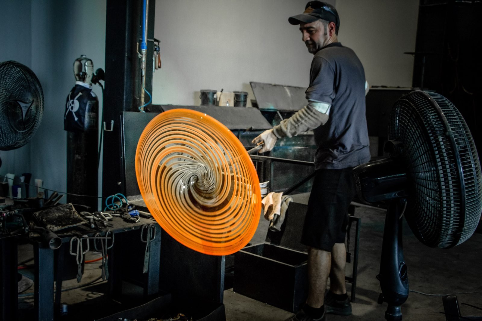 Peça circular de cristal laranja com desenho em espiral sendo girada no ateliê