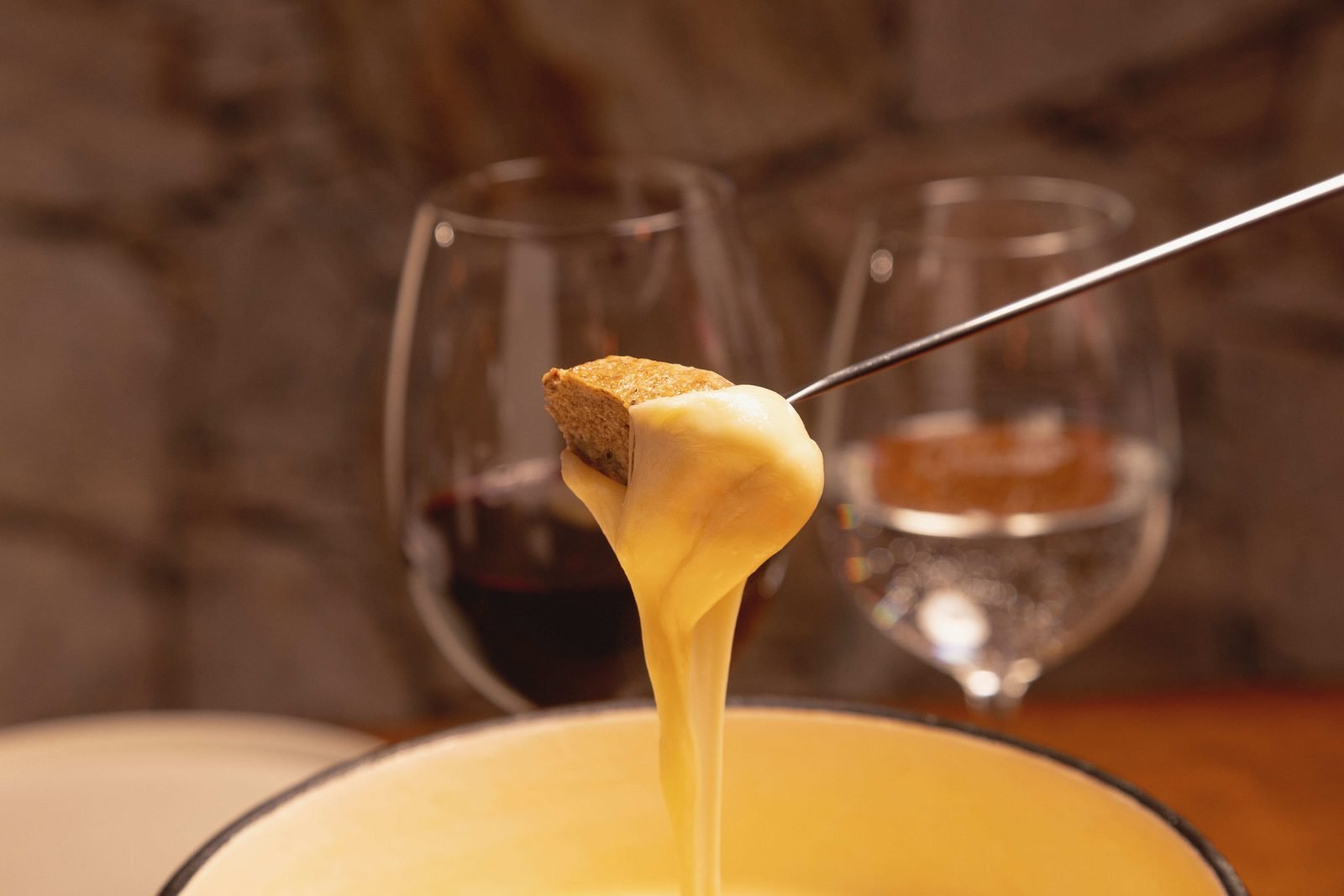 Cubo de pão puxando fio de queijo derretido acima da panela de fondue