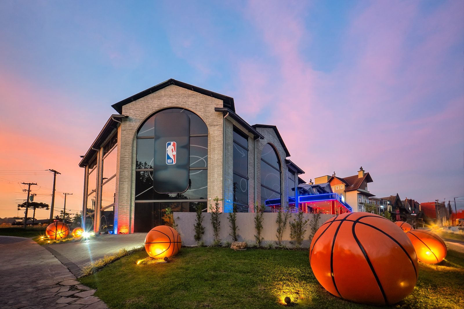 Fachada do NBA Park Gramado ao entardecer, com esculturas de bolas de basquete no gramado