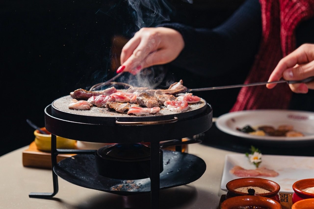 Pedra quente com cortes de carne sendo preparados à mesa
