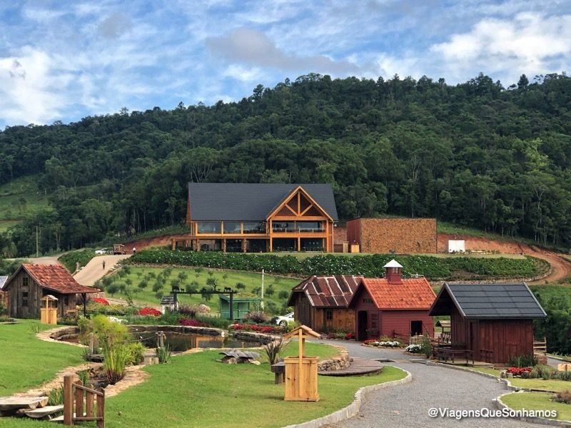 Casas antigas de madeira e lago no parque, com o prédio principal ao fundo na encosta