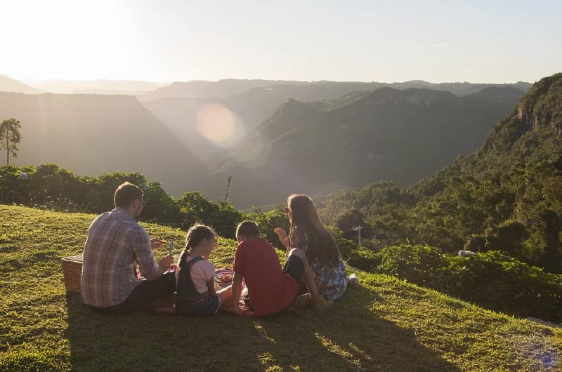 Família sentada na grama diante do cânion durante o pôr do sol