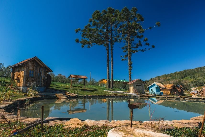 Casinhas de madeira em volta de um lago, com araucárias ao fundo
